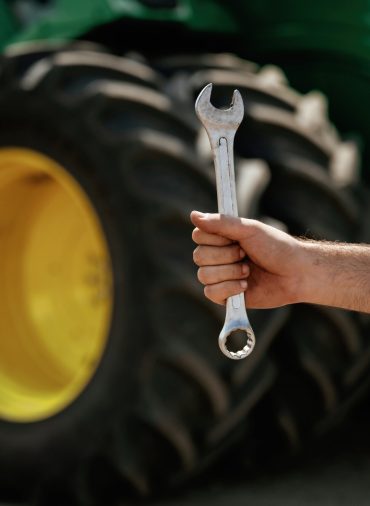 Close-up of hand holding wrench in front of tractor.
