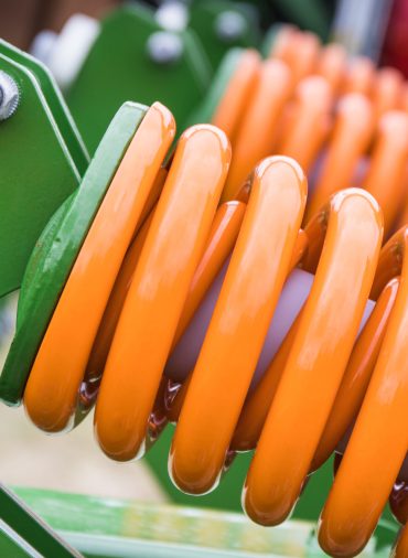 Orange hard spring made of steel. Detail and part of big industrial or agricultural machine. Technology
